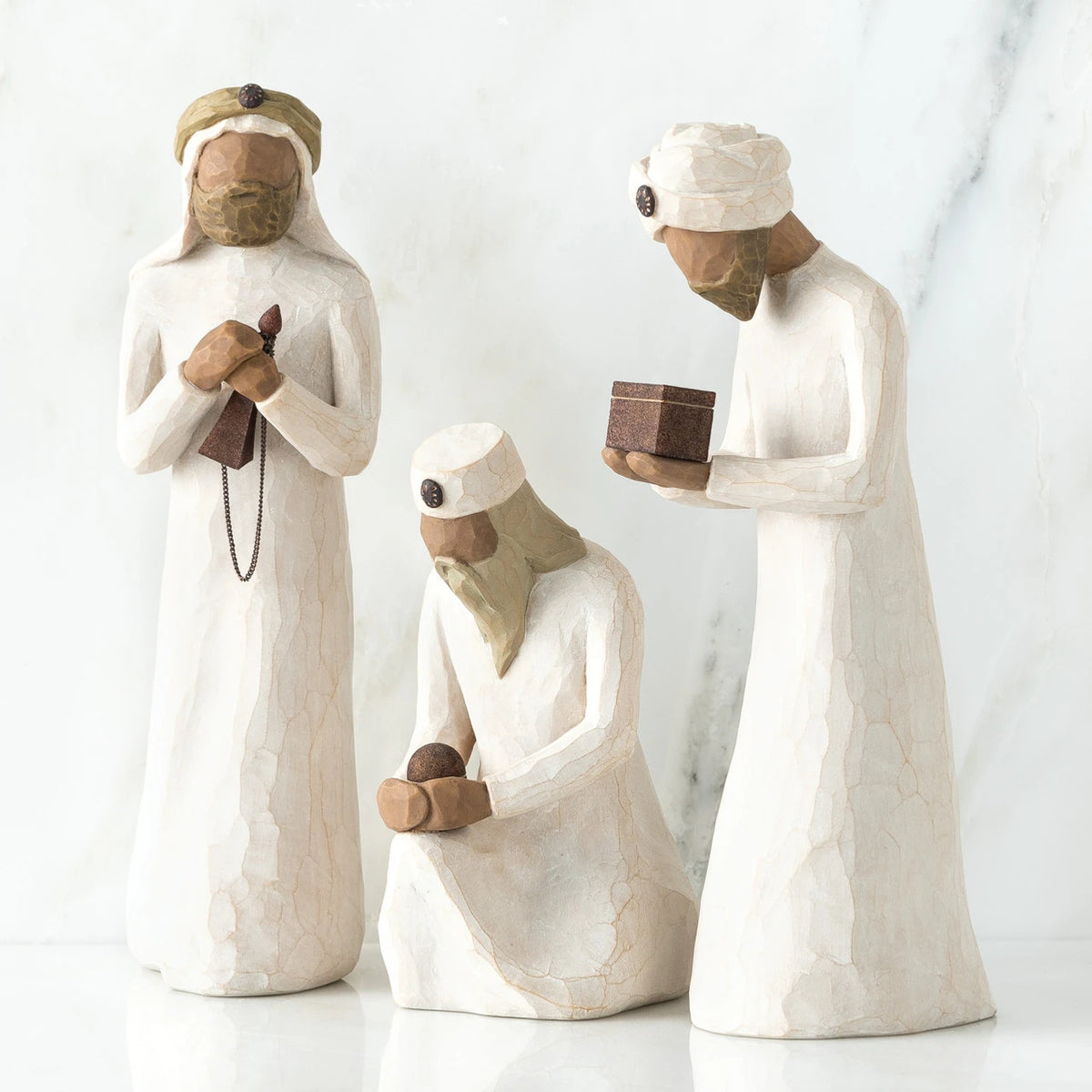 Set of three wiseman figurines -two are standing - far right one standing is holding brown box - one is sitting in the middle holding a rock