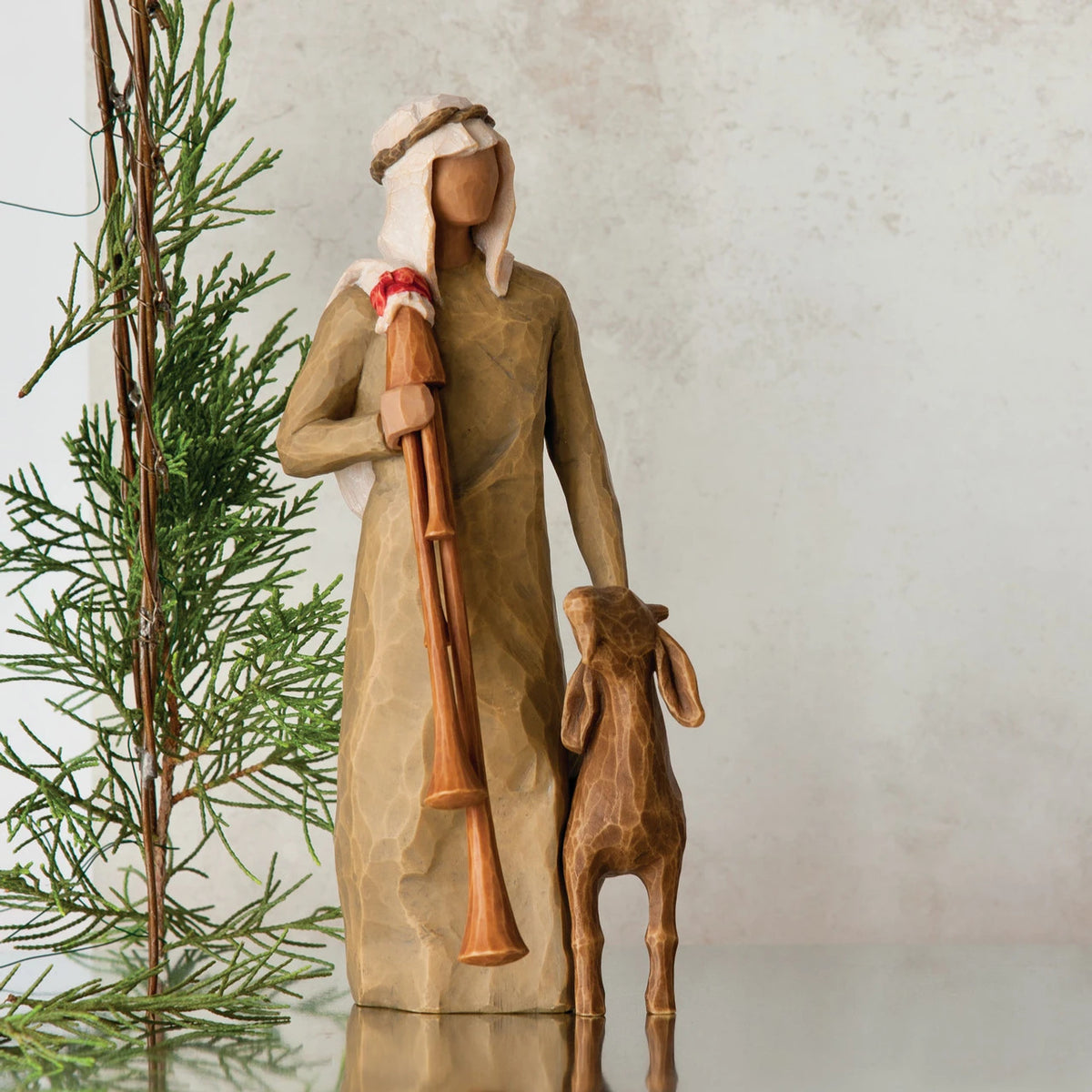 Wiseman figurine in tan dress next to golden lamb figurine with green tree in the background